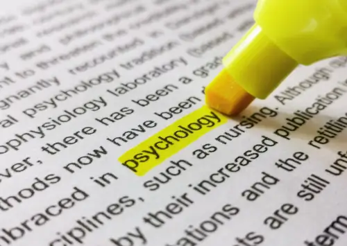 Close-up image of a marker highlighting the word "psychology" in a book.